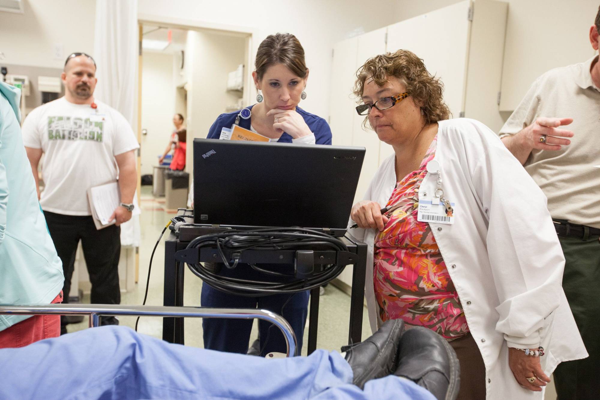 A faculty member and a student glance at a screen. A simulation patient exercise is happening.